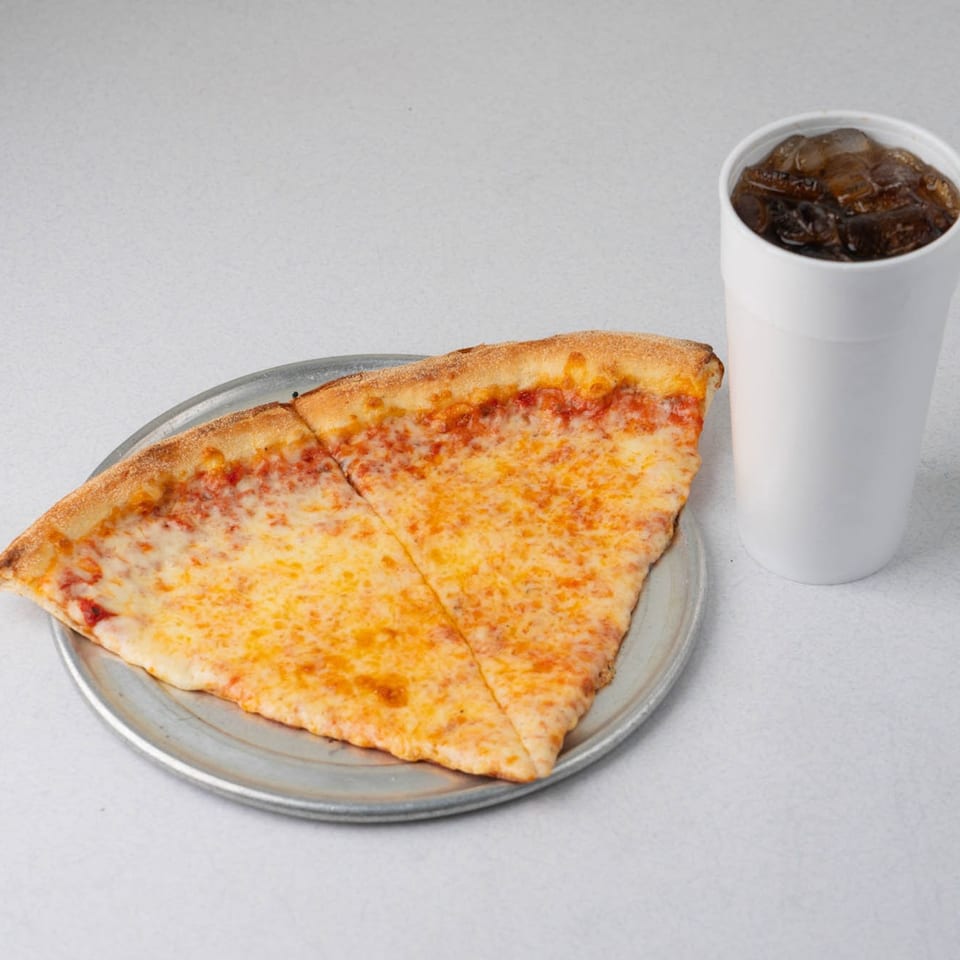 Two slices of TJ's cheese pizza on a metal pan with a white cup of soda.