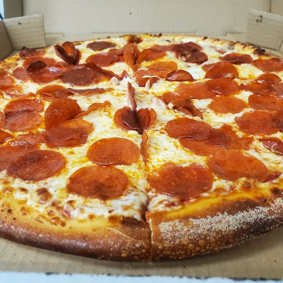 A whole pepperoni pizza from TJ's Pizza & Wings, with melted cheese and a golden crust, in a box.